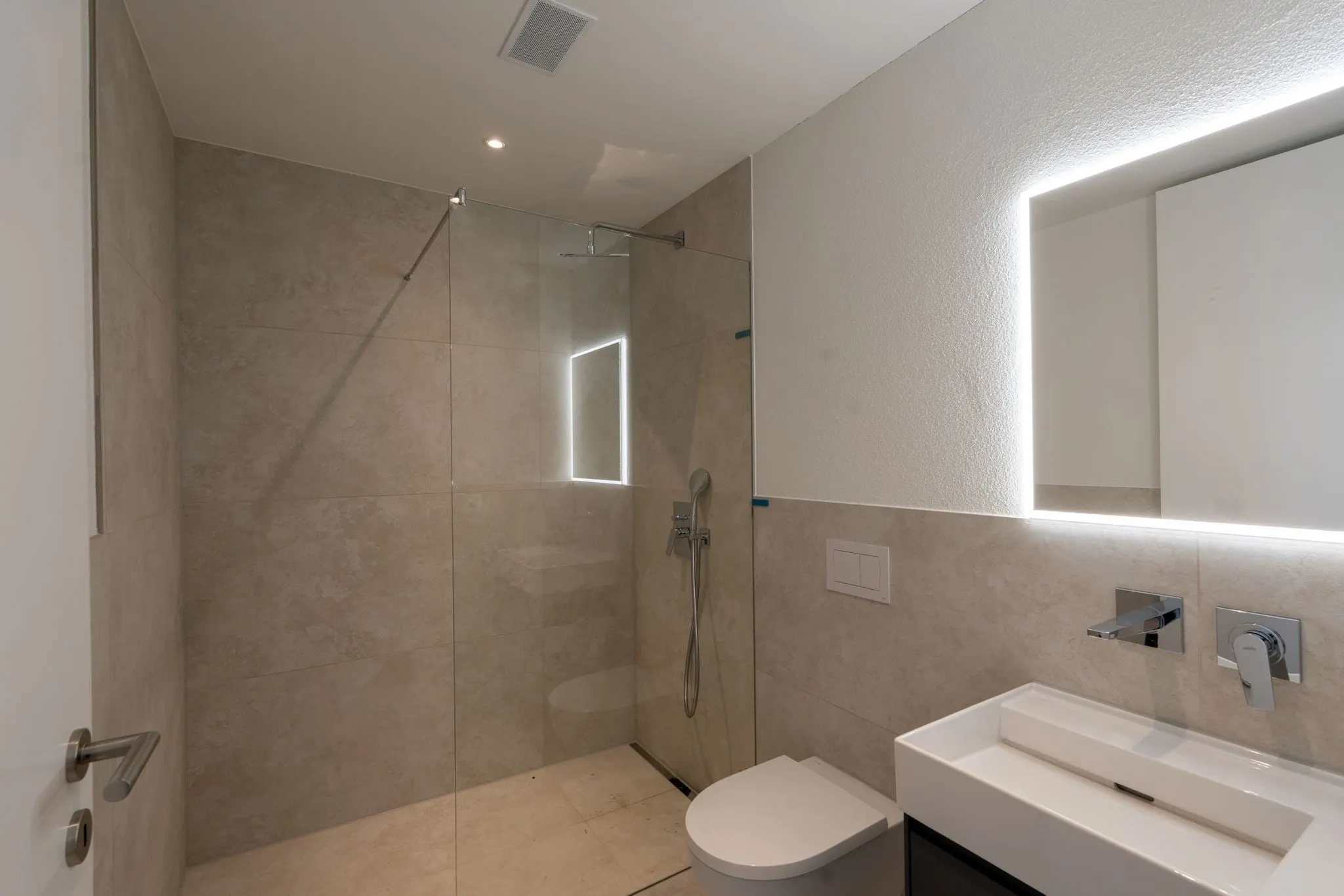 Badezimmer mit Dusche und beleuchtetem Spiegel